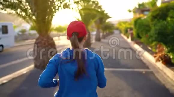 日落时分女人沿着街道在棕榈树之间奔跑后景健康的生活方式视频的预览图
