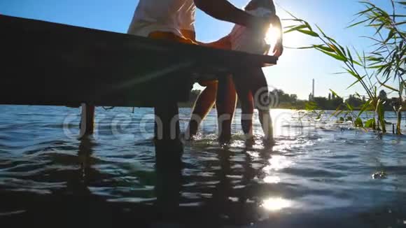 父亲手牵着儿子坐在湖边的木码头边把腿悬在水里小可爱视频的预览图