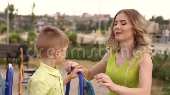 小可爱的男孩在公园的操场上玩耍时亲吻他的妈妈视频的预览图