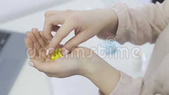 年轻女子手里拿着许多黄色的小药丸把一颗药丸放进嘴里和小手视频的预览图