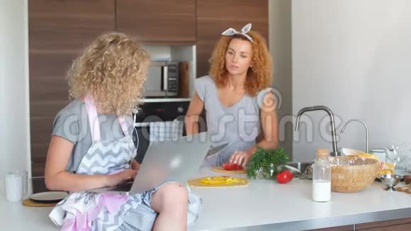 小女孩和她的女儿在家烤饼干在笔记本电脑上阅读食谱视频的预览图