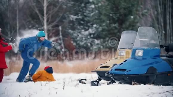 冬季森林快乐的一家人穿着五颜六色的衣服在雪地摩托附近玩雪球慢动作视频的预览图