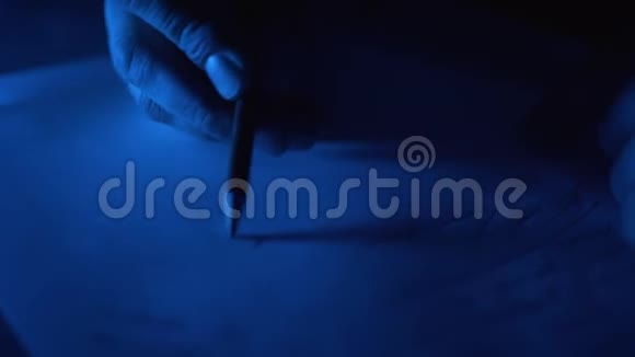 男人在房间里的一张纸上写字一只雄性手在深蓝色的光线下写在纸上视频的预览图
