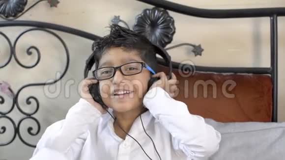可爱的印度亚裔白人小男孩戴着眼镜戴着耳机欣赏音乐手放在耳朵上坐在李视频的预览图
