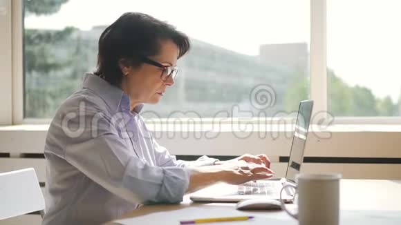 从侧面看女商人正在家里工作场所使用笔记本电脑视频的预览图