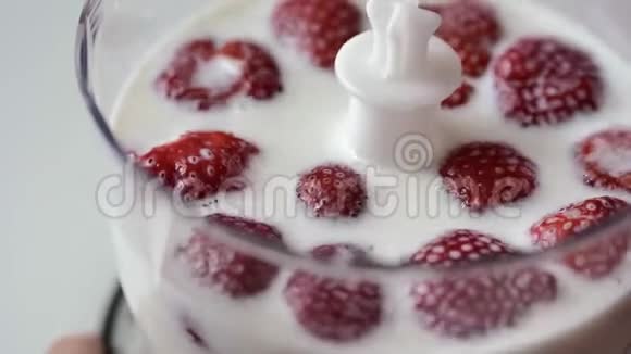 在搅拌机下面的透明杯中牛奶草莓漂浮特写视频的预览图