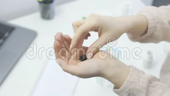 女人拿着两个黑色的药丸喝着办公室里的玻璃水视频的预览图