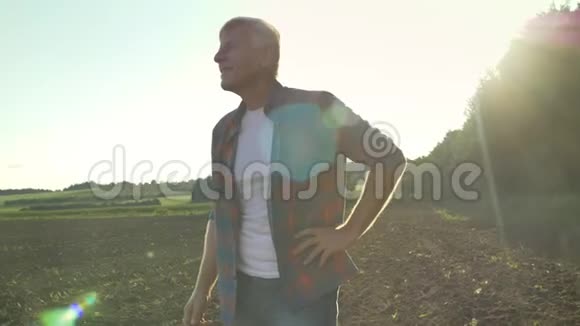 快乐的老农夫穿着衬衫站着用愉快的表情看着他的田野美丽的自然景观视频的预览图