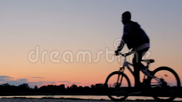 清晨日出时一个骑自行车的人骑在河边体育生活方式少年的剪影视频的预览图