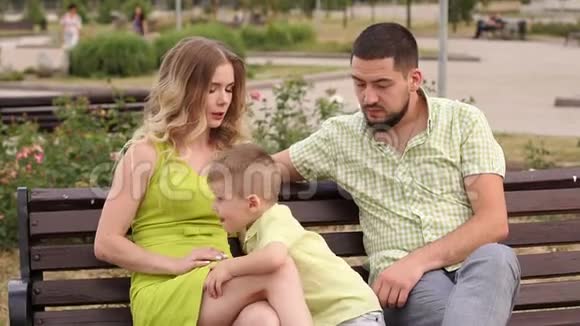 快乐的年轻家庭他的儿子在夏天在公园里的长凳上休息视频的预览图
