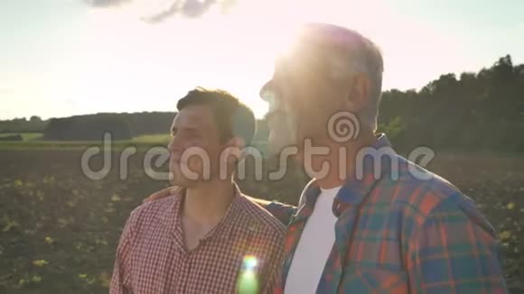 老爸爸抱着儿子看着耕种的田地日落时美丽的背景镜头耀斑视频的预览图