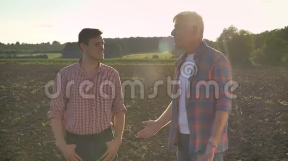 快乐的老父亲向儿子展示了耕种的田地在夕阳的背景下微笑着美丽的自然视频的预览图