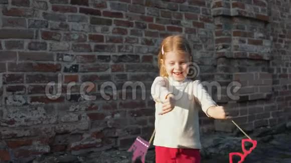 小女孩拿着一个纸眼镜和一根棍子上的皇冠站在砖墙旁边视频的预览图