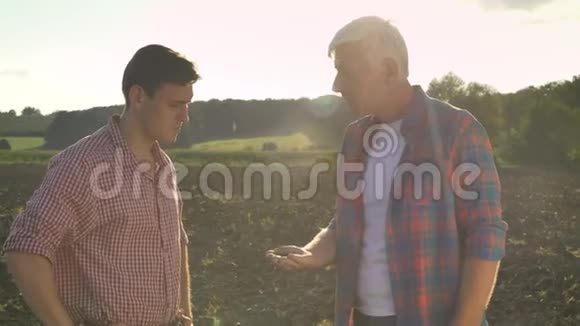 父亲和儿子在说话爸爸拿着泥土在手掌上说话站在田野上夕阳和美丽视频的预览图
