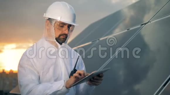 体贴的太阳能工人正站在夕阳下的太阳能装置旁边拿着一台电脑视频的预览图
