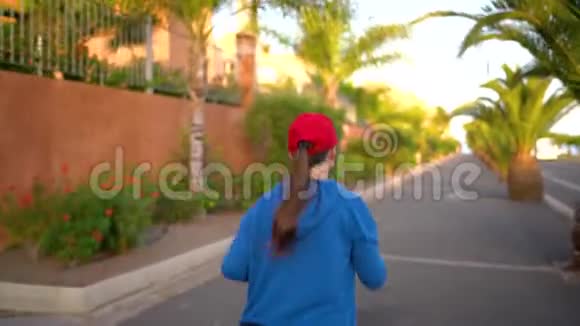 日落时分女人沿着街道在棕榈树之间奔跑后景健康的生活方式视频的预览图