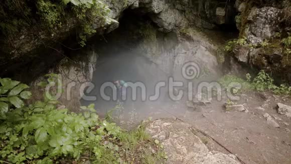 旅行者潜入洞穴库存录像带保险的探险者沿着陡峭的下坡进入岩石中的黑雾洞穴视频的预览图