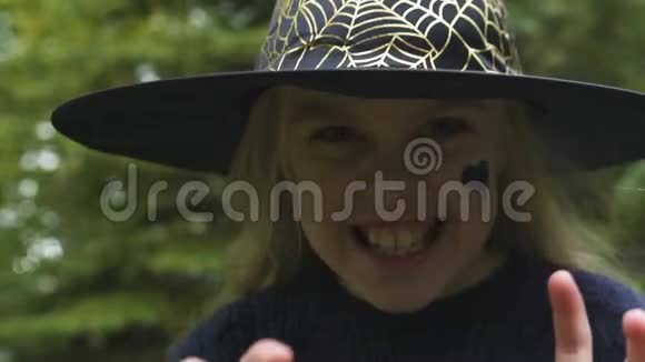 可爱的小女孩穿着女巫的服装制作恐怖的面部摄像头假装魔法视频的预览图