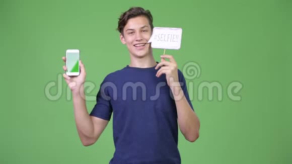 年轻英俊的十几岁男孩展示电话和自拍纸标志视频的预览图