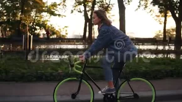 迷人的女孩骑自行车在早晨公园或林荫大道一位穿休闲服装的年轻女子骑着一辆视频的预览图