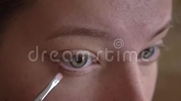 年轻的白种人女化妆师在她的下眼皮上涂一把刷子的特写照片视频的预览图
