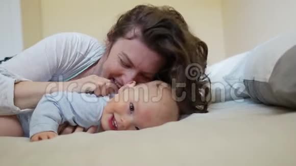美丽的卷曲女人亲吻和拥抱一个一岁的孩子妈妈和孩子挠痒痒笑视频的预览图