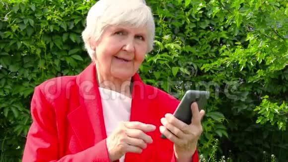 老太太的肖像祖母在太阳日在户外使用电话现代奶奶的手指触摸她的手机触摸屏视频的预览图
