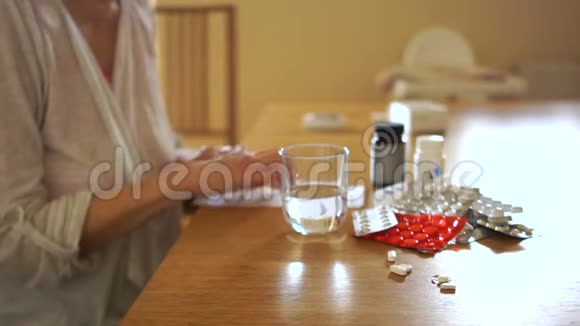 关节炎女人一边吃药一边喝水一边坐在桌旁视频的预览图