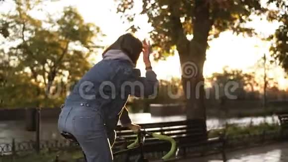 美丽的女性骑自行车在早晨公园或林荫大道一个穿着蓝色牛仔裤骑着徒步自行车的年轻女子视频的预览图