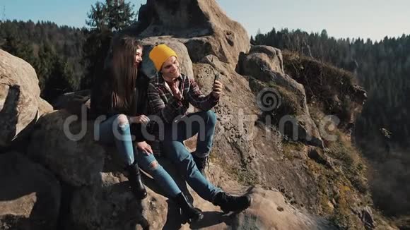 恋爱中的年轻夫妇坐在岩石上和朋友视频聊天旅游交流休息聊天理念视频的预览图