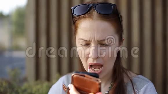 一位中年妇女坐在街头咖啡馆的餐桌旁用智能手机而不是智能手机涂口红视频的预览图