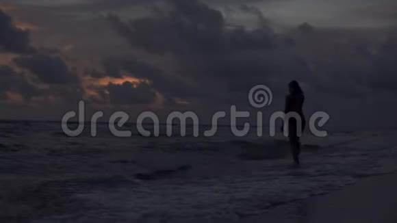日落时分一位年轻的金发女郎沿着大海走着视频的预览图