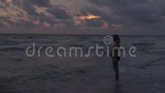 日落时分一位年轻的金发女郎沿着大海走着视频的预览图