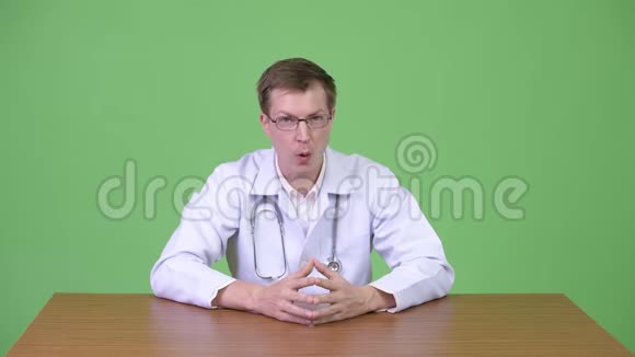 年轻的自信男医生坐着微笑说话视频的预览图