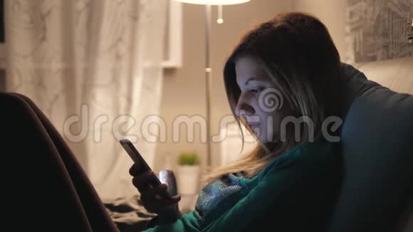 在家睡觉前躺在床上的女人使用你的电话应用程序视频的预览图