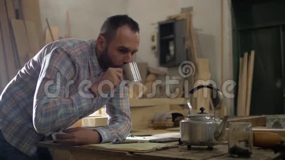 一个留着胡子的人在木工车间喝茶做计算视频的预览图