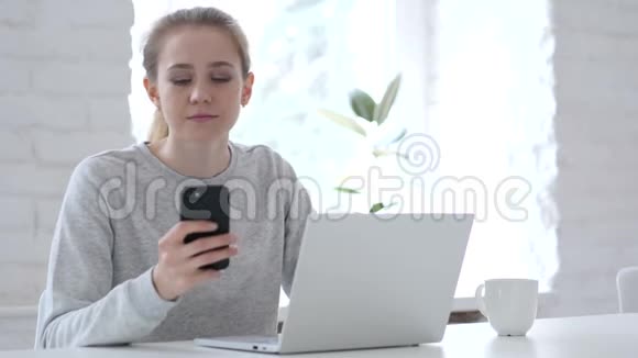 年轻女子在手提电脑时使用智能手机视频的预览图