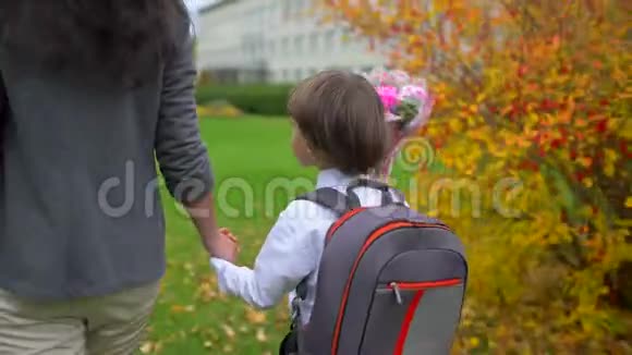 母亲牵着小儿子的手背着背包去户外上学一年级学生小学第一视频的预览图