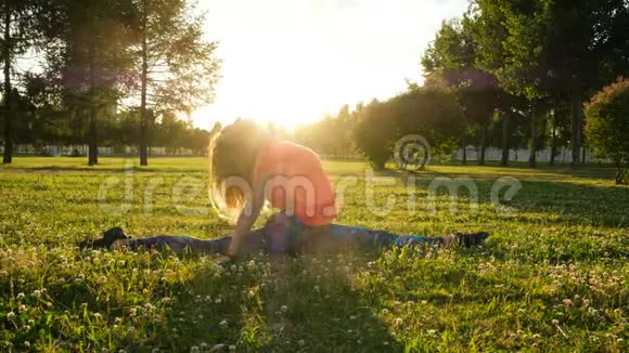 女体操运动员坐在自然公园草地上的树枝上转身伸展身体视频的预览图