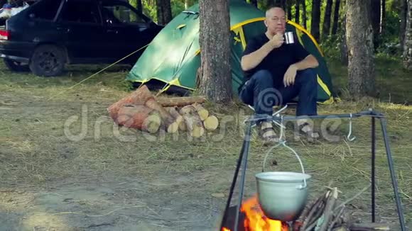 那人正在帐篷附近喝茶看着锅挂在火堆上视频的预览图