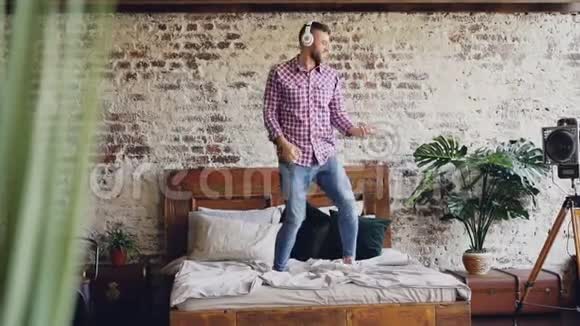 大胡子帅哥在床上跳着舞戴着耳机听音乐动作很慢现代阁楼视频的预览图