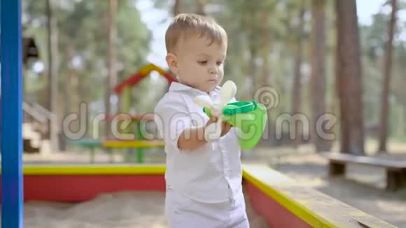 有趣的小男孩夏天站在公园的沙箱里独自玩塑料玩具视频的预览图