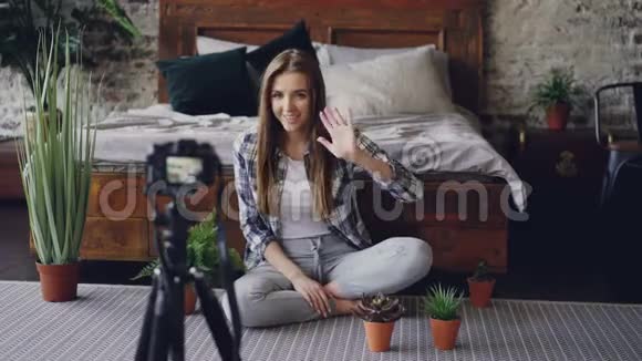 美丽的女孩受欢迎的博客作者录制了一段关于房子花的视频相机坐在靠近双人床的地板上视频的预览图