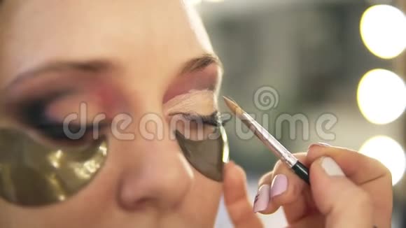 化妆师在模特的眼睛上涂上浅色的眼影闭合补丁侧视图视频的预览图
