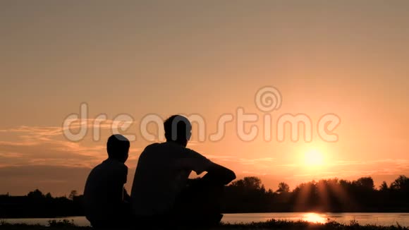 两个人在河岸或湖边交流的剪影父子俩坐在水边看着视频的预览图