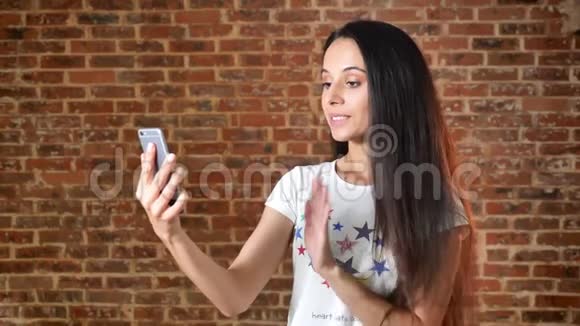 年轻可爱的女孩使用智能手机令人惊讶背景砖墙肖像视频的预览图