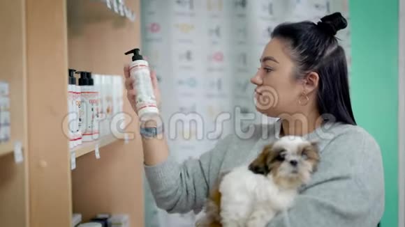 一位年轻的女宠物主人正在一家商店里为她的狗挑选洗发水手里拿着可爱的狮子狗视频的预览图