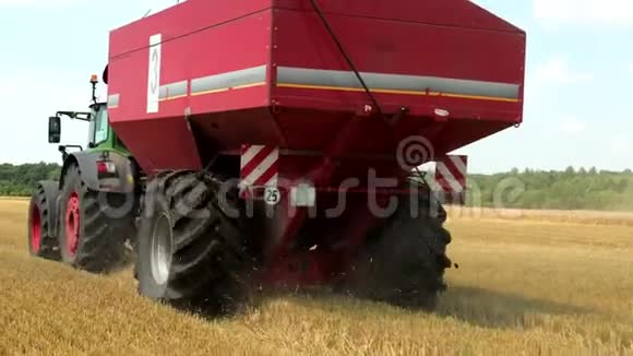 绿色拖拉机与一个红粮槽在田野上行驶在收获道具慢动作视频的预览图
