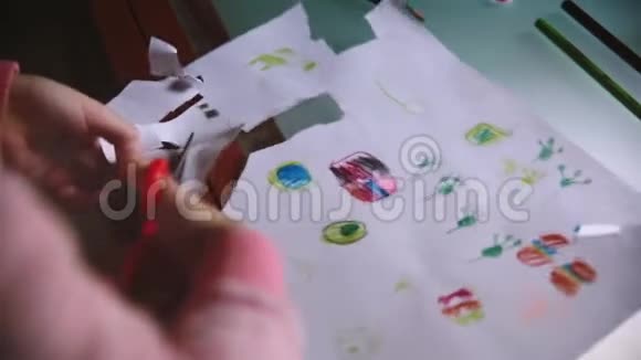 一个可爱的小女孩的特写镜头她用剪刀在桌子上从一张纸上剪出手绘图片视频的预览图