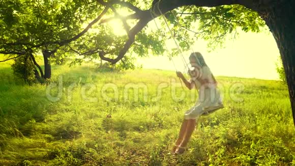 快乐的女孩长发在树枝上摆动在公园里荡秋千的快乐女孩慢动作视频的预览图